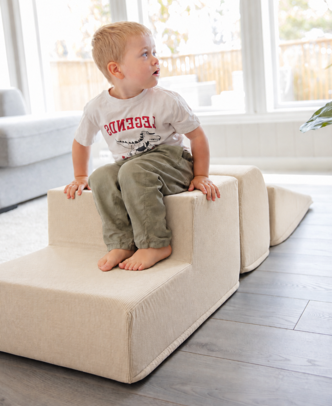 Barfot gutt i hvit T-skjorte sitter på Trollefant skumblokker i beige cord i lys stue med sofa og store vinduer