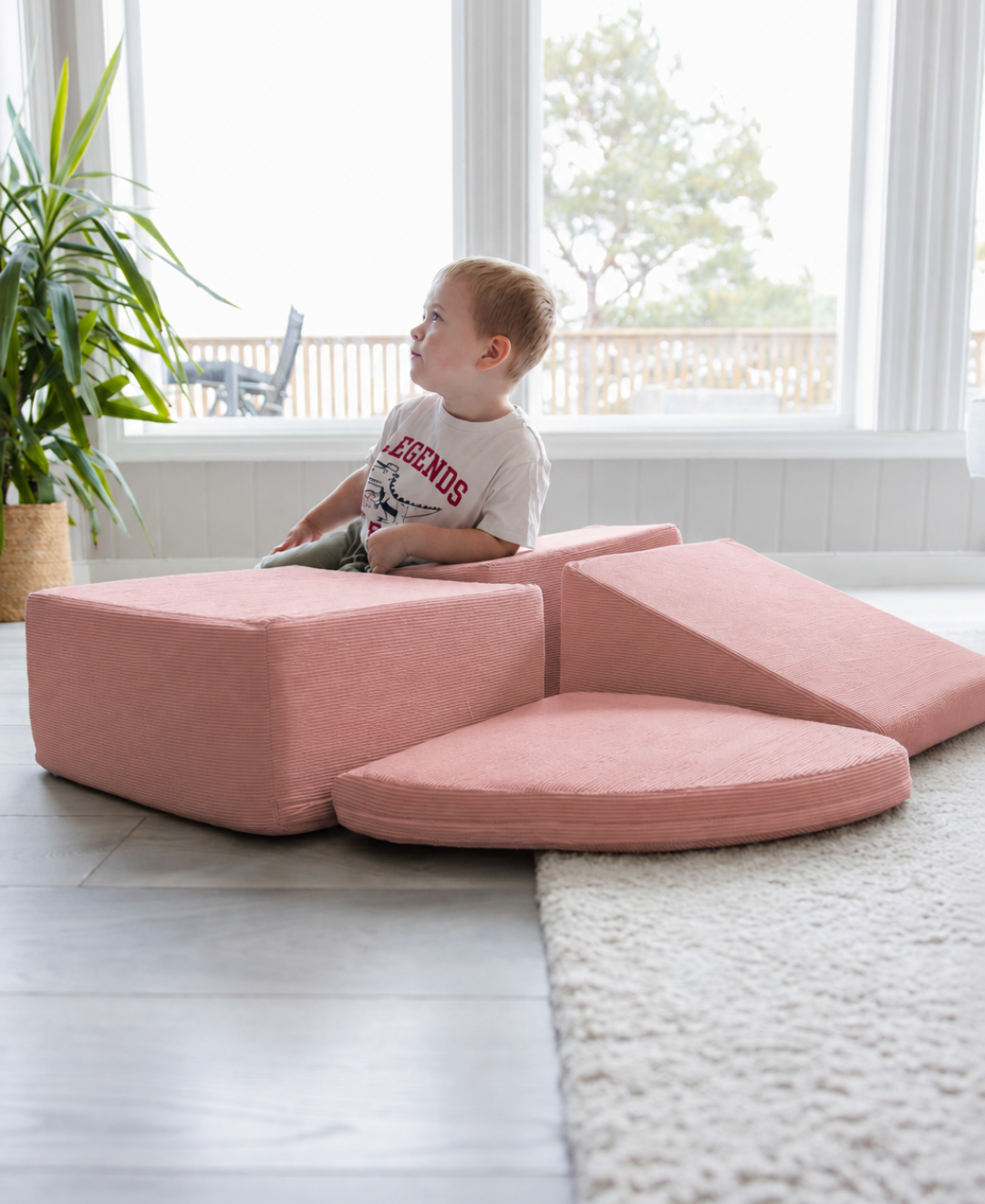 Gutt sitter på Trollefant skumblokker i rosa cord, satt opp som borg foran lyse vinduer på grått gulv med hvit teppekant